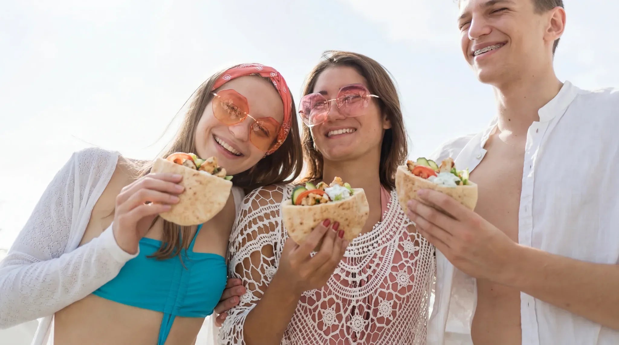 Three friends enjoying pita bread outdoors on a sunny day.